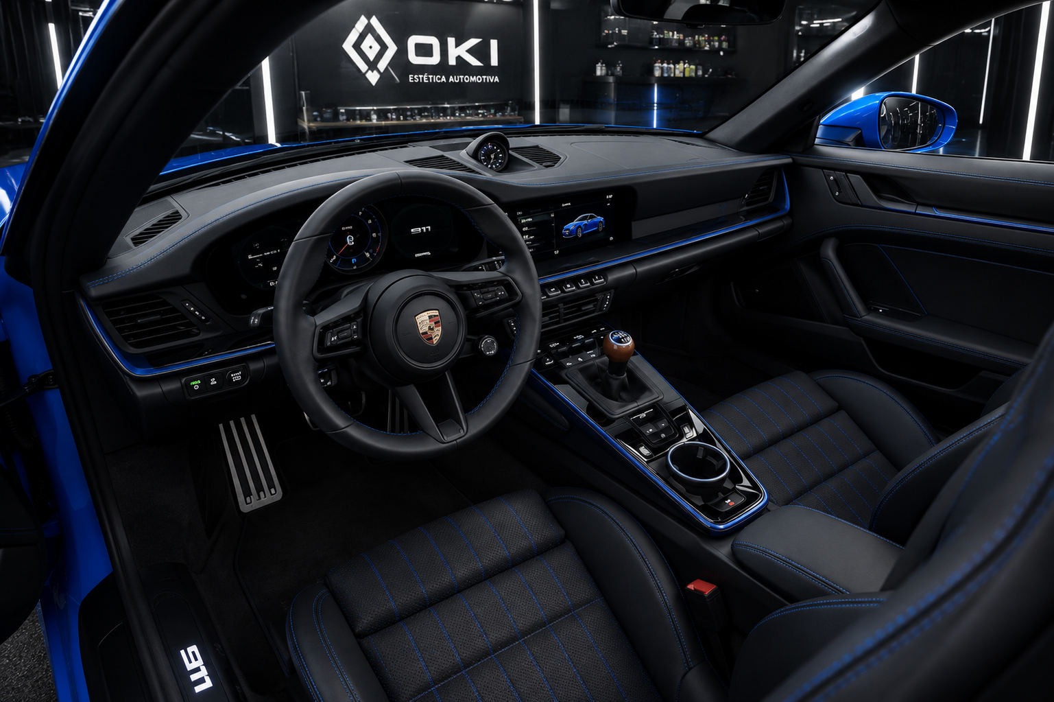 Interior do Porsche 911 azul em estúdio OKI, mostrando volante, painel, console central e bancos com detalhes azuis